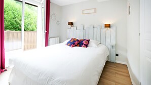A bedroom with a large bed, a view through a sliding door, and a white headboard with wall-mounted lights. - Holiday Apartment "Escapade Au Pays Basque 2 to 4 Guests" with Balcony, Shared Garden & Wi-Fi (Urrugne)