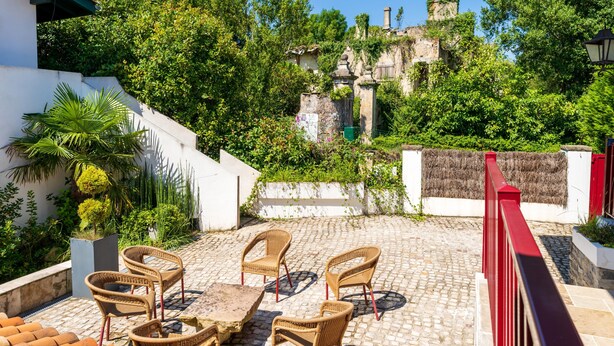 A patio with wicker furniture, cobblestone flooring, and a view of greenery and buildings in the background. - Holiday Apartment "Escapade Au Pays Basque 2 to 4 Guests" with Balcony, Shared Garden & Wi-Fi (Urrugne)