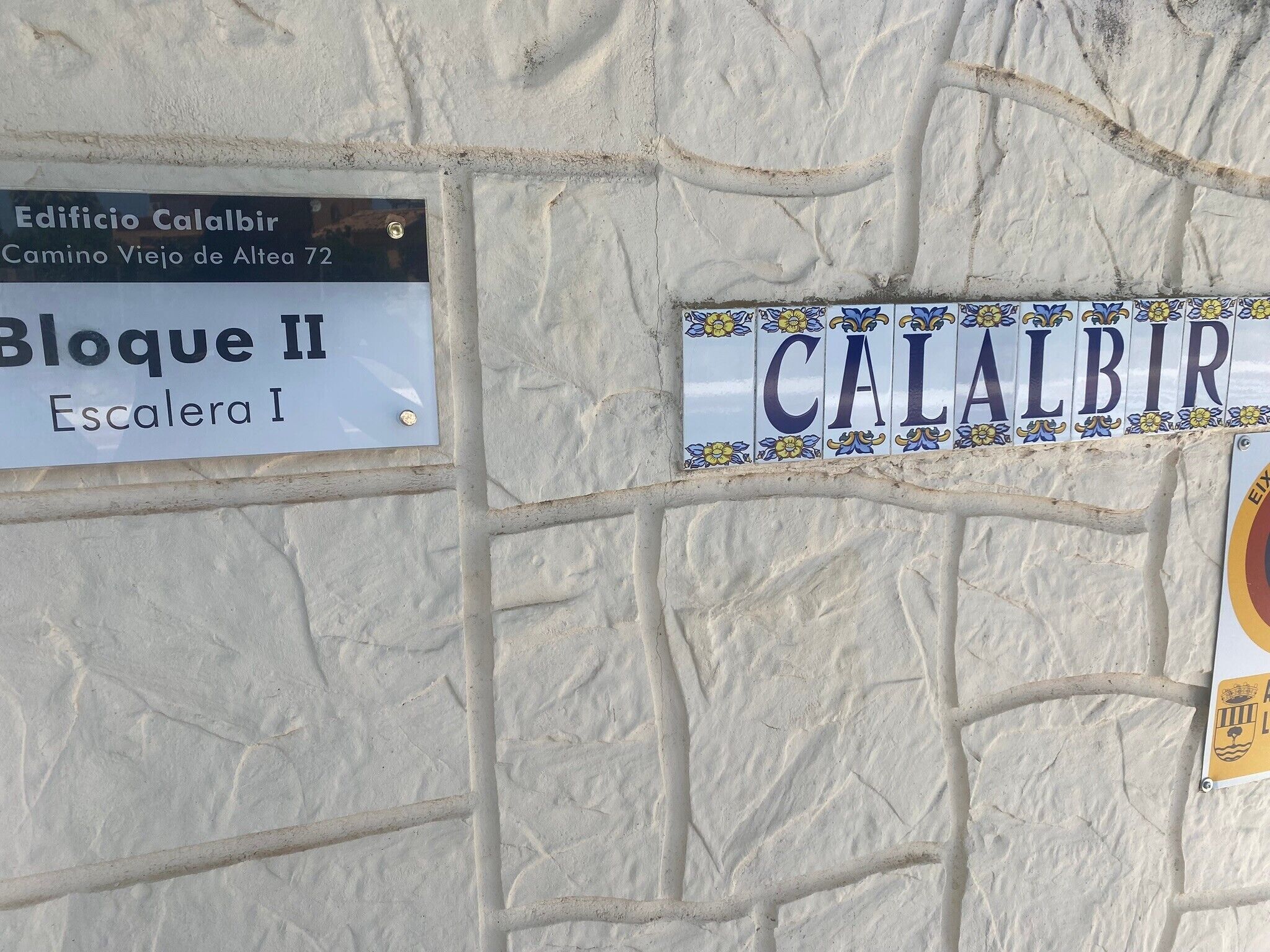 Señales de calle que indican 'Edificio Calalbir' y 'Escalera I' sobre un muro con textura.