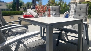 A table with a bottle, glasses, and a vase of flowers. There are chairs with cushions around the table. - Apartment 'Apartamento Cal Albir' with Shared Pool, Wi-Fi and Air Conditioning (l'Alfàs del Pi)