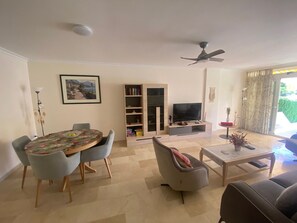 A living room with a dining table, chairs, a sofa, a TV, a bookshelf, and a ceiling fan. - Apartment 'Apartamento Cal Albir' with Shared Pool, Wi-Fi and Air Conditioning (l'Alfàs del Pi)