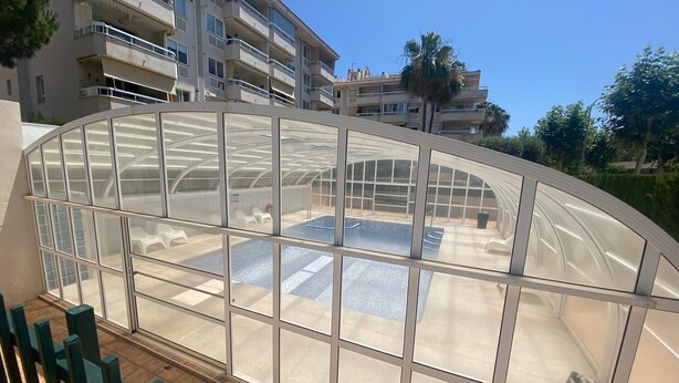 A glass-enclosed pool area with a view of a multi-story building in the background. - Apartment 'Apartamento Cal Albir' with Shared Pool, Wi-Fi and Air Conditioning (l'Alfàs del Pi)