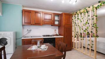 Una cucina funzionale con mobili in legno, una lavatrice, un tavolo da pranzo con sedie e un letto separato da un pannello in legno.
