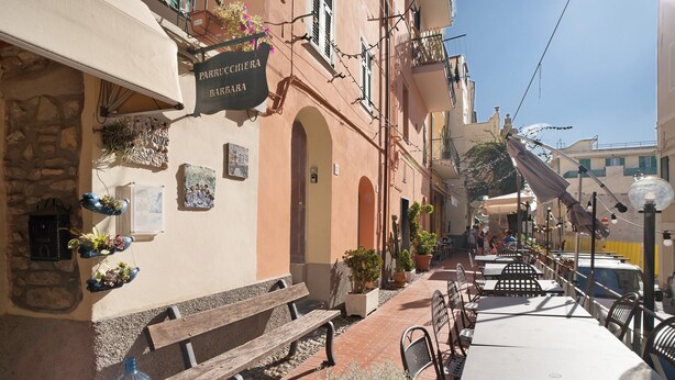 A narrow street with outdoor seating, stone walls, and a sign for 'PARRUCCHEA BARBA.'