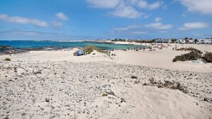 A beach with scattered rocks, a few umbrellas, and buildings in the background.