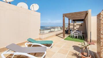 Una terraza en la azotea con sillones de descanso, una pérgola, una planta en maceta y vistas al mar.
