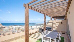 A terrace with a wooden pergola, a table with chairs, and a view of the beach and ocean.