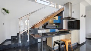 A modern kitchen with a central island, a built-in stove, and a staircase leading to an upper level.