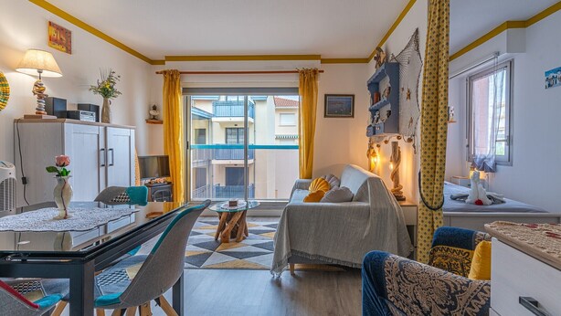 A well-lit living room with a sofa, a dining table, and a TV. There is a balcony visible through the door. - Studio Apartment 'Cabine Centre Ville' with Wi-Fi (ARCACHON)