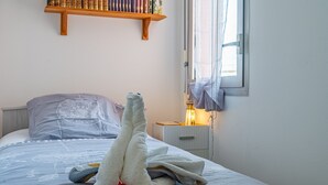 A bed with a white towel and a rose, a bedside table with a lamp, and a bookshelf above the bed. - Studio Apartment 'Cabine Centre Ville' with Wi-Fi (ARCACHON)