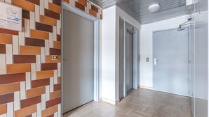 A hallway with a patterned wall, a closed door, an elevator, and a plain door. - Studio Apartment 'Cabine Centre Ville' with Wi-Fi (ARCACHON)