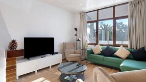 Un salon moderne avec un téléviseur à écran plat, un canapé vert, un fauteuil beige et une table basse ronde.