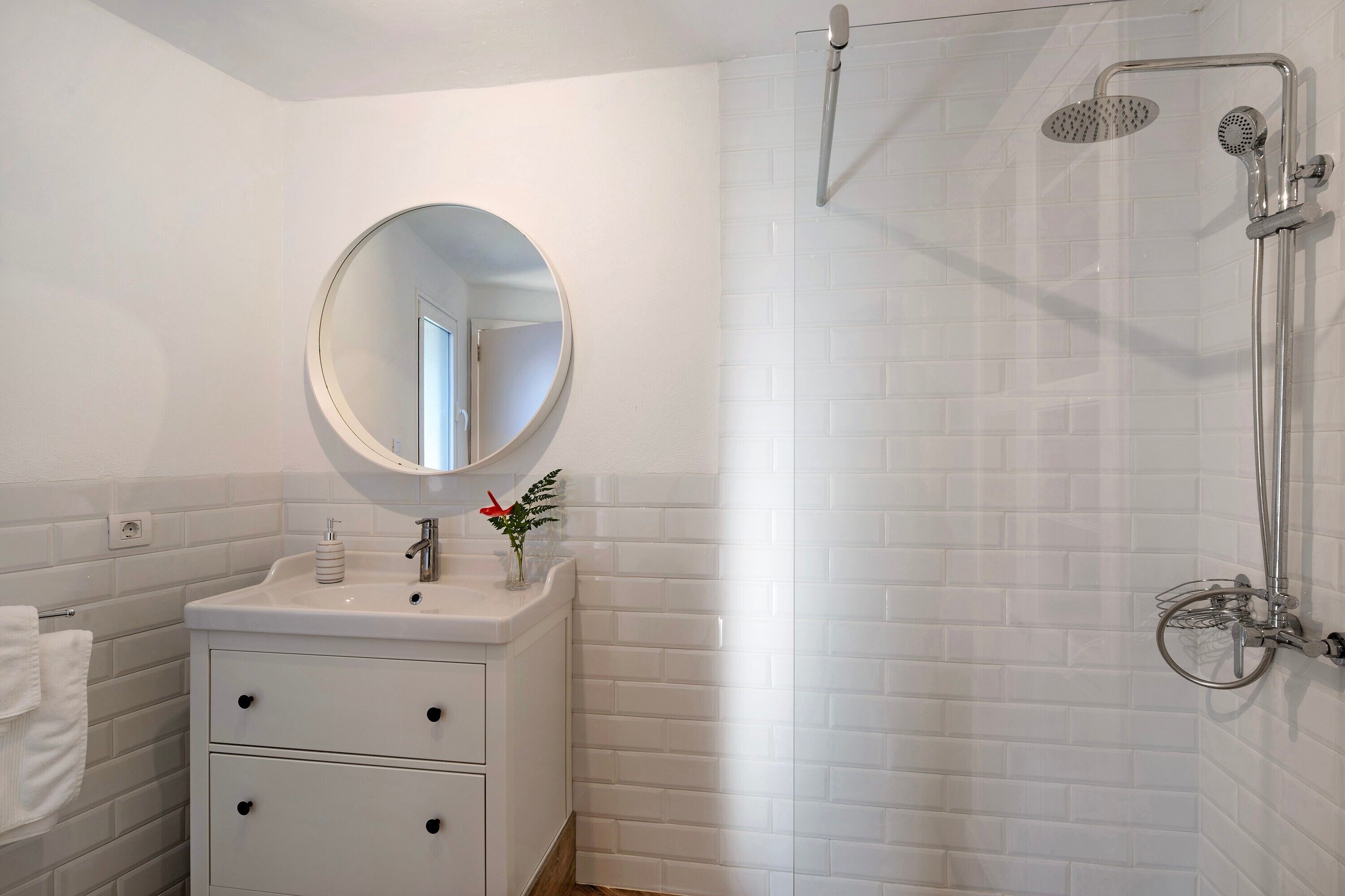 Un baño con lavamanos blanco, espejo redondo y ducha con cabezal de ducha de mano.