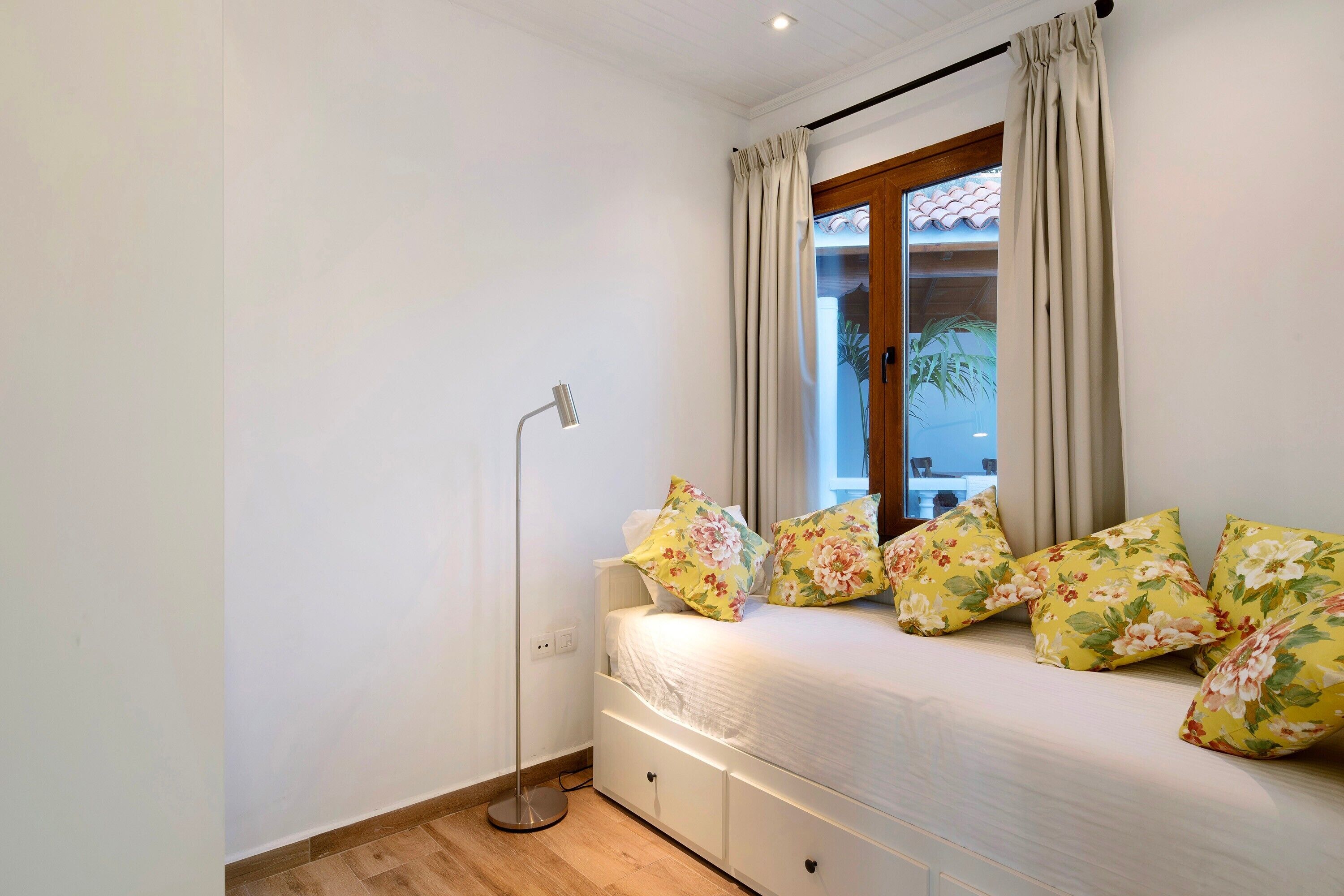 Een slaapkamer met een bed, een vloerlamp en een raam met gordijnen.