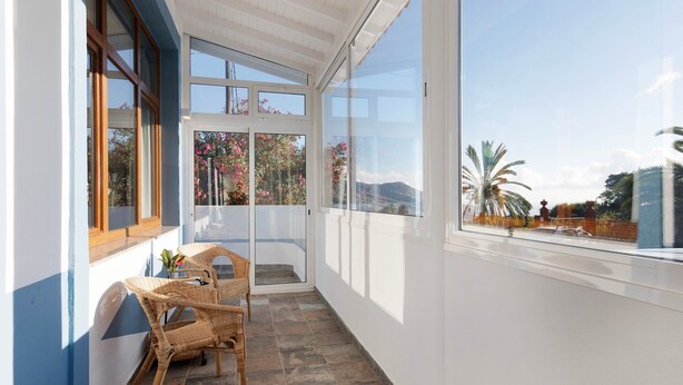 Un balcon agrémenté de meubles en osier, une porte vitrée donnant sur une terrasse et une vue sur les arbres et les montagnes.