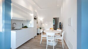Una cocina moderna con armarios blancos, una zona de comedor con una mesa redonda y sillas, y un ventanal.