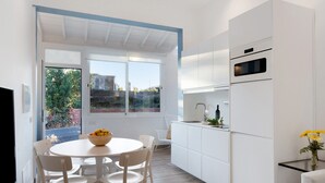 Una cocina moderna con armarios blancos, una mesa de comedor con sillas y vistas a través de un ventanal.