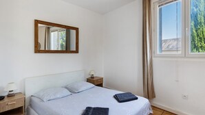 Ein Schlafzimmer mit einem Bett, einem Nachttisch, einer Lampe, einem Spiegel und einem Fenster mit Vorhängen.