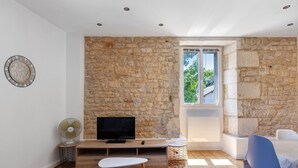 A modern room with a stone wall, a flat-screen TV, a fan, a dining area, and a window with a view. - Studio Apartment "5 - 3 Min Du Futuroscope" with Wi-Fi (Chasseneuil du Poitou)