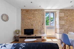A modern room with a stone wall, a flat-screen TV, a fan, a dining area, and a window with a view. - Studio Apartment "5 - 3 Min Du Futuroscope" with Wi-Fi (Chasseneuil du Poitou)