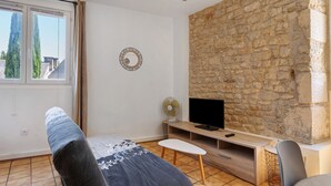 Ein Zimmer mit Steinwand, einem Fernseher auf einem Holztisch, einem Ventilator und einem Fenster mit Vorhängen.