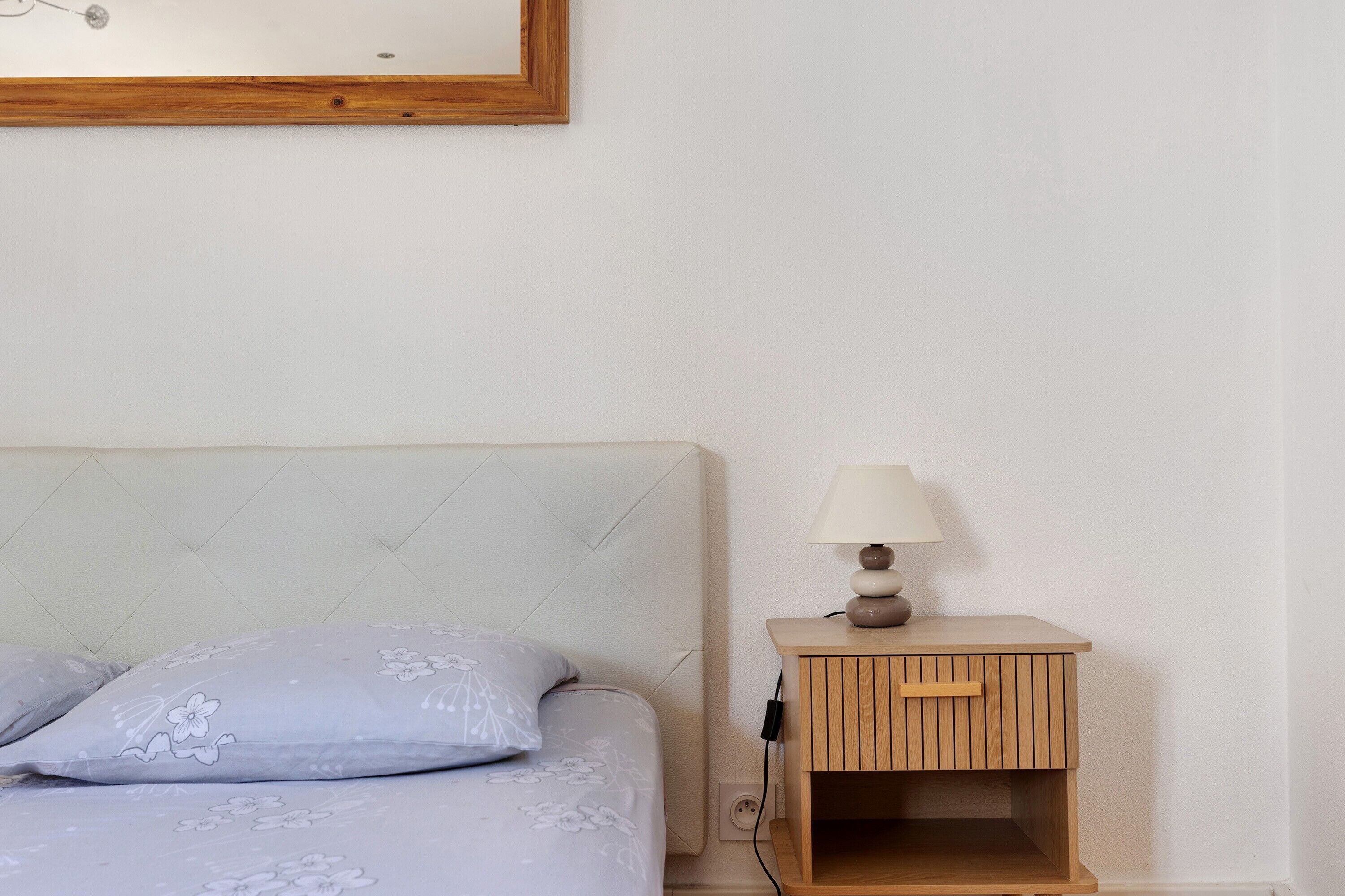 Een bed met een bloemenprintdeken, een nachtkastje met een lamp en een houten nachttafeltje.