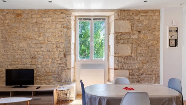 A room with a stone wall, a round table with chairs, a television, and a window with a view of trees. - Studio Apartment "5 - 3 Min Du Futuroscope" with Wi-Fi (Chasseneuil du Poitou)