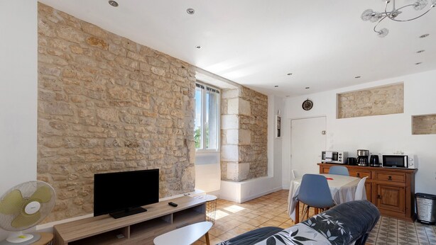 Ein modernes Wohnzimmer mit Steinwand, Flachbildfernseher, Sofa, Esstisch und Küchenzeile mit Geräten.
