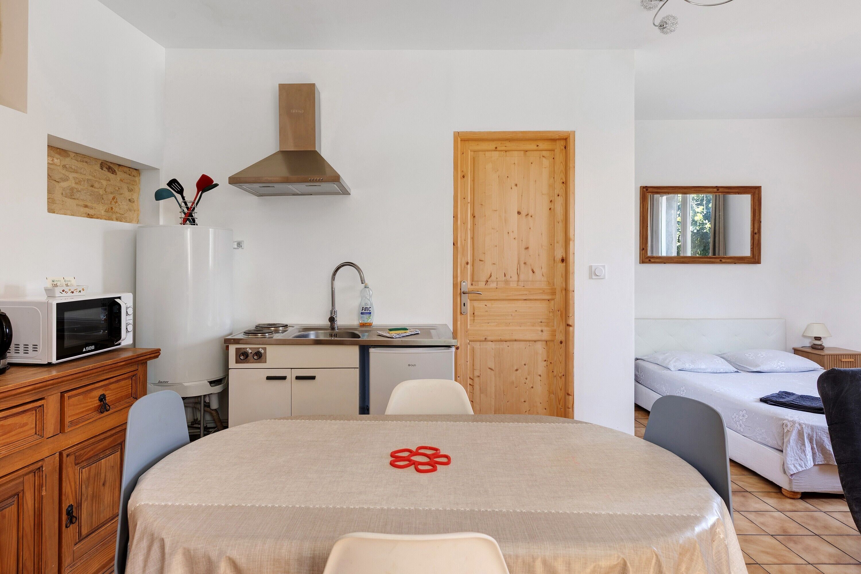 Habitación funcional con mesa, microondas, lavamanos, puerta de madera, cama y ventana.