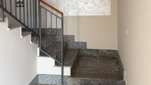 Eine Treppe mit Handlauf, einer Leuchte darüber und einer gemusterten Matte am Fuß.