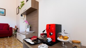 Ein Hotelzimmer mit einem roten Sofa, einer Kaffeemaschine, einem Tablett mit Frühstücksartikeln, einem Glas und einem gerahmten Bild an der Wand.