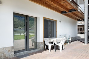 Un portico coperto con tavolo e sedie, una porta scorrevole in vetro e vista su un paesaggio montuoso.