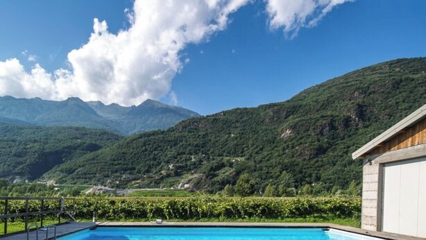 Una piscina con vistas a la montaña, un edificio de madera y un muro de piedra.