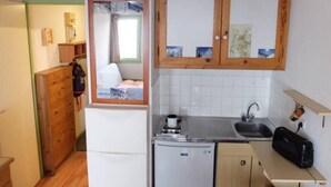 Pieni, käytännöllinen keittiö, jossa on puukaapit, pieni jääkaappi, pesuallas ja leivänpaahdin.