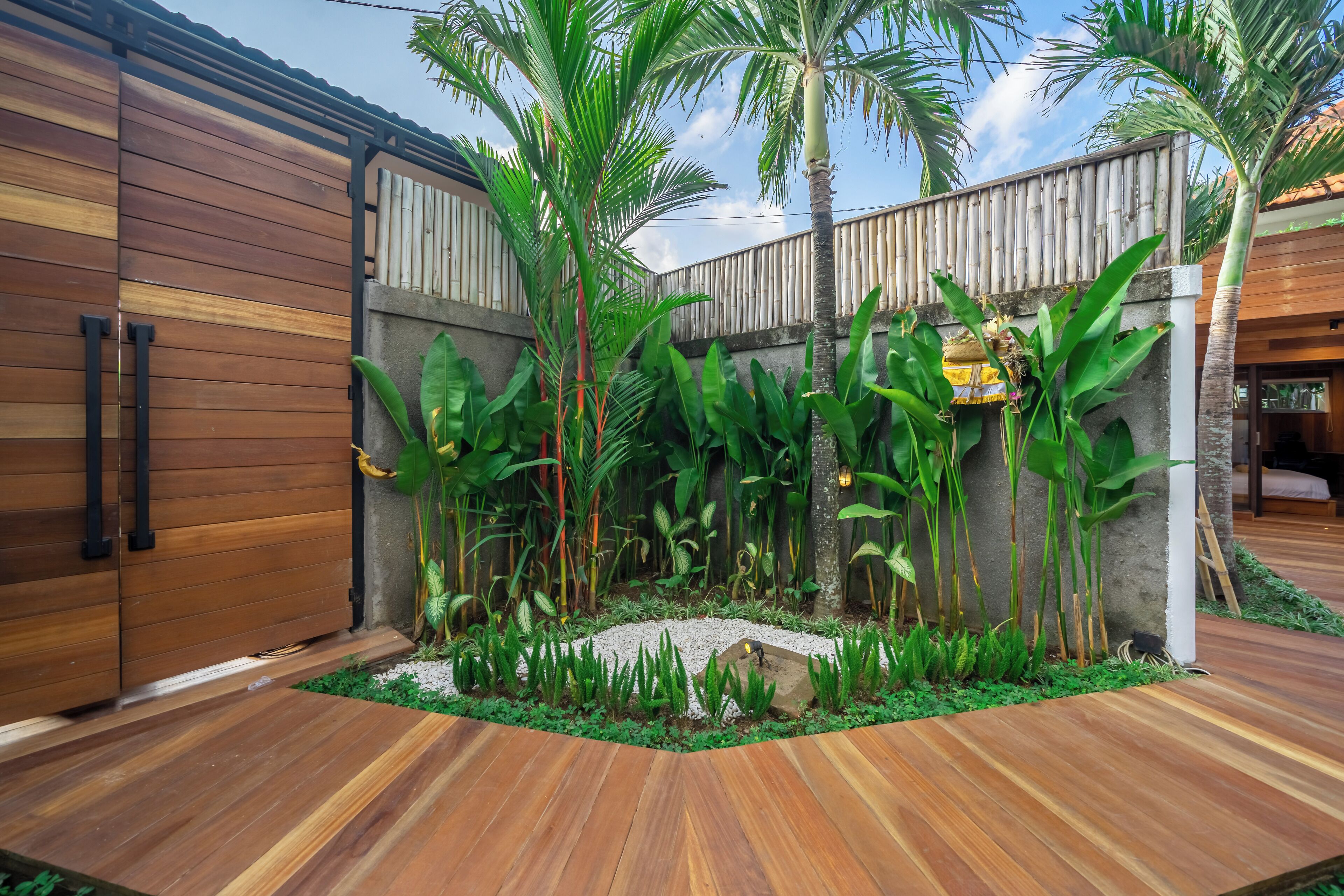 A modern house with a wooden exterior, a concrete wall, and a garden with tropical plants and a small pond.