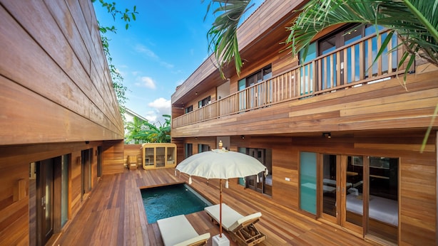 A wooden deck with a pool, lounge chairs, and an umbrella. - ZenDen (Tibubeneng)