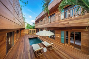 Una terraza de madera con piscina, sillas de descanso y una sombrilla.
