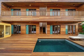 A modern two-story building with a wooden exterior, a swimming pool, and a balcony with a wooden railing. - ZenDen (Tibubeneng)