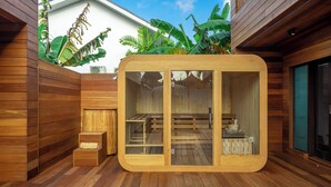 A wooden sauna with glass doors, a wooden deck, and a white building in the background. - ZenDen (Tibubeneng)