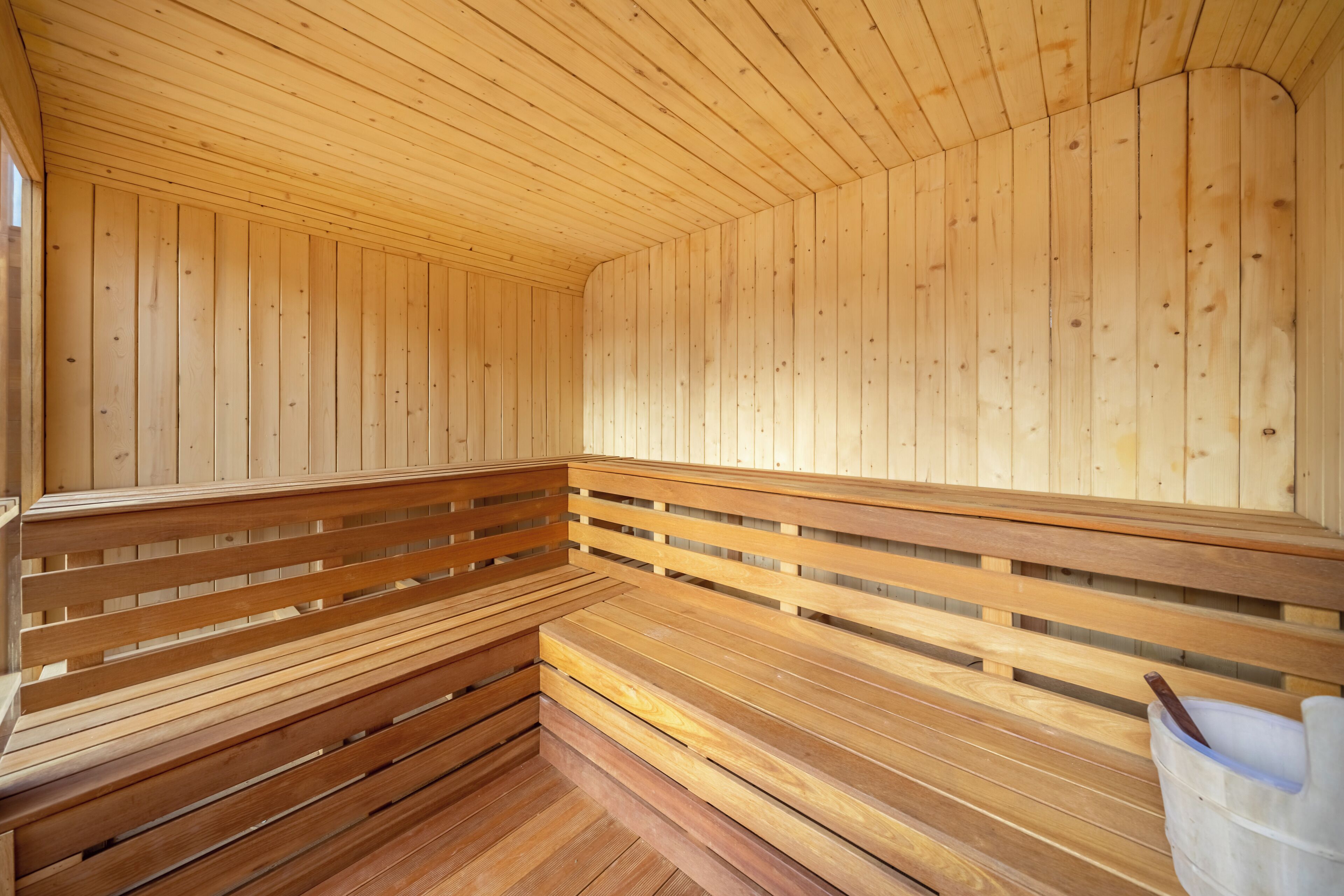 A wooden sauna with benches and a bucket of stones.