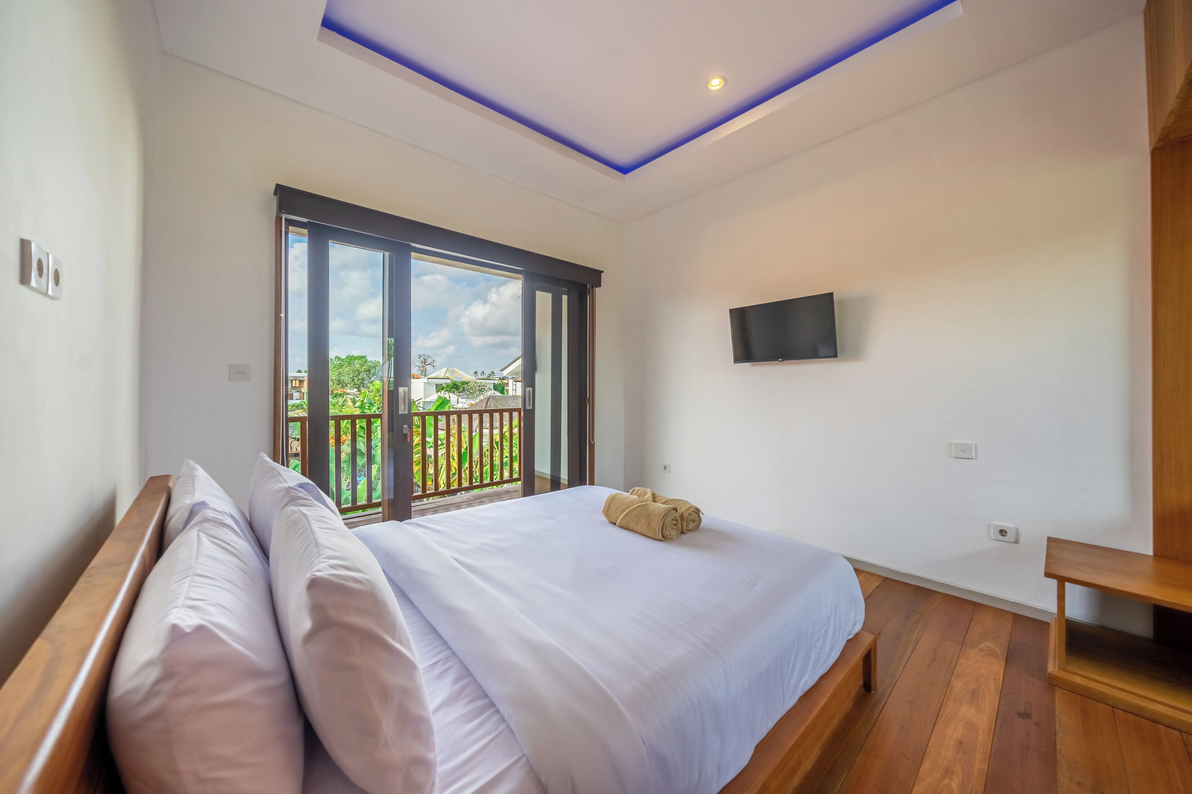 Un dormitorio con una cama grande, un televisor montado en la pared y un balcón con vistas a zonas verdes.