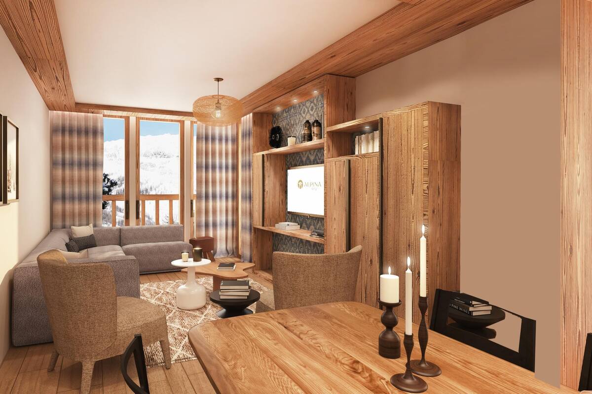 Ein gemütliches Wohnzimmer mit einem Holzesstisch, einer Couch und einem Couchtisch. An den Wänden hängen Bilder in Rahmen, und ein Bücherregal beherbergt dekorative Gegenstände.