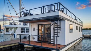 A modern floating home with a deck, a staircase, and a sign reading 'FLOHOM 02 MODERN CHARM'.
