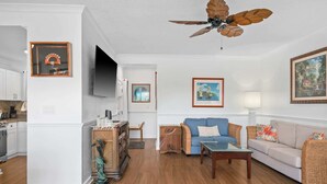 A living room with a wooden floor, a blue sofa, a wooden coffee table, a television, and framed artwork on the walls.