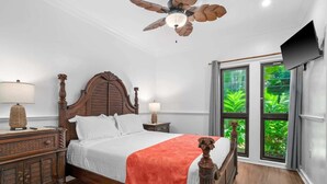 A bedroom with a wooden bed, two bedside tables, a ceiling fan, and a TV on the wall.