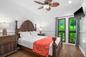 A bedroom with a wooden bed, two bedside tables, a ceiling fan, and a TV on the wall. - Ocean Views W/Full-Kitchen Await - Kaha Lani #104 (LIHUE, KAUAI)
