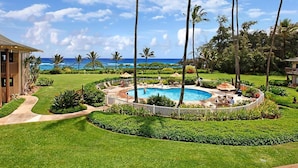 A pool surrounded by palm trees and a view of the ocean. - Ocean Views W/Full-Kitchen Await - Kaha Lani #104 (LIHUE, KAUAI)