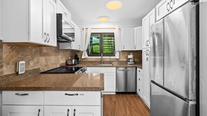 A modern kitchen with white cabinets, stainless steel appliances, a built-in oven, and a window with a view of greenery.