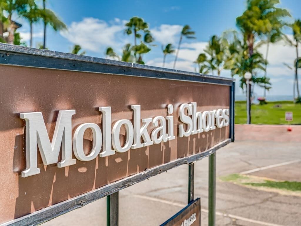 A sign for Molokai Shores with a clear view of the surrounding palm trees and a pathway.