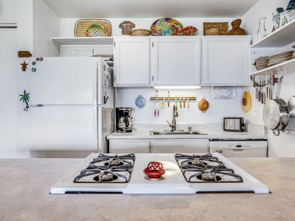 A kitchen with white cabinets, a stove, and various kitchen utensils.